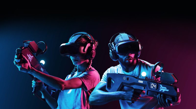 Two VR gamers wearing VIVE Focus 3 HMDs hold Zero Latency VR laser tag style weapons