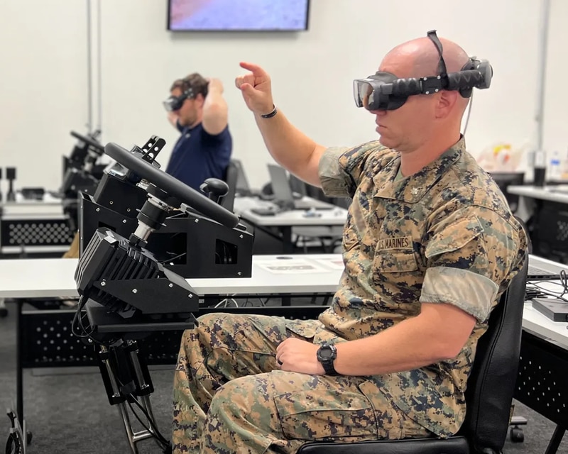 a US Marine wearing a VIVE XR Elite HMD uses hand gestures to navigate menu options in a XRT ACV driving simulator